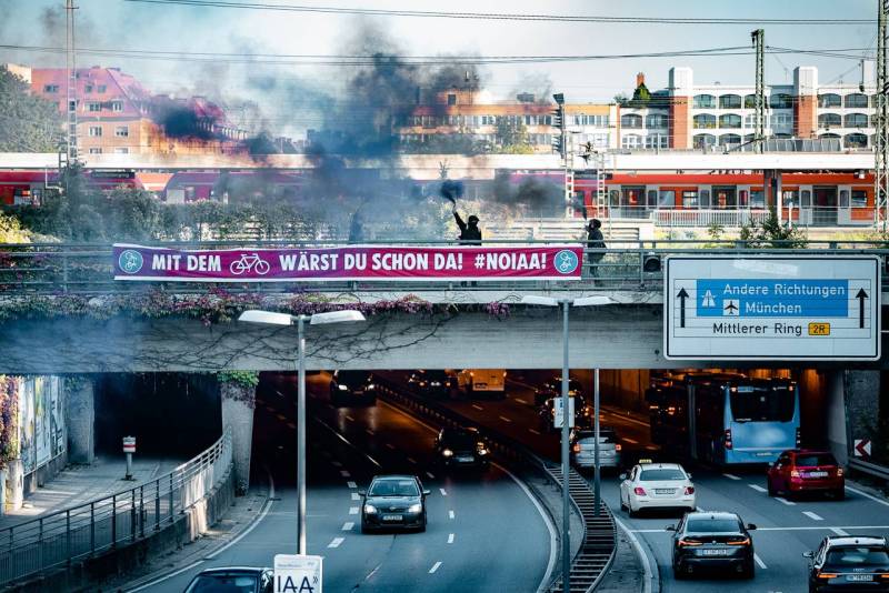 Antikapitalistisches Klapprad Kollektiv (AKK) läutet Beginn der Proteste gegen die IAA in München ein! Am Mittleren Ring  wurde auf einer Brücke über dem allmorgendlichen Stau ein zehn Meter langes Transparent im Stile eines Fahrradweges befestigt mit dem Text "Mit dem Rad wärst du schon da #NoIAA".